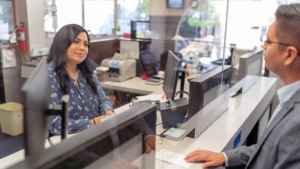 A professional bank teller assisting a customer at a counter, processing transactions, and providing friendly customer service.